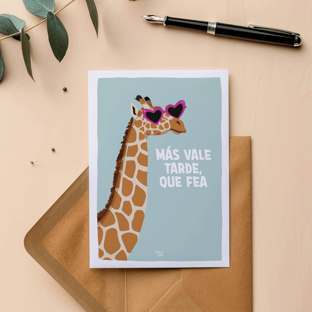 Postal ilustrada con una jirafa y texto gracioso colocada encima de un sobre de papel. Más vale tarde, que fea.