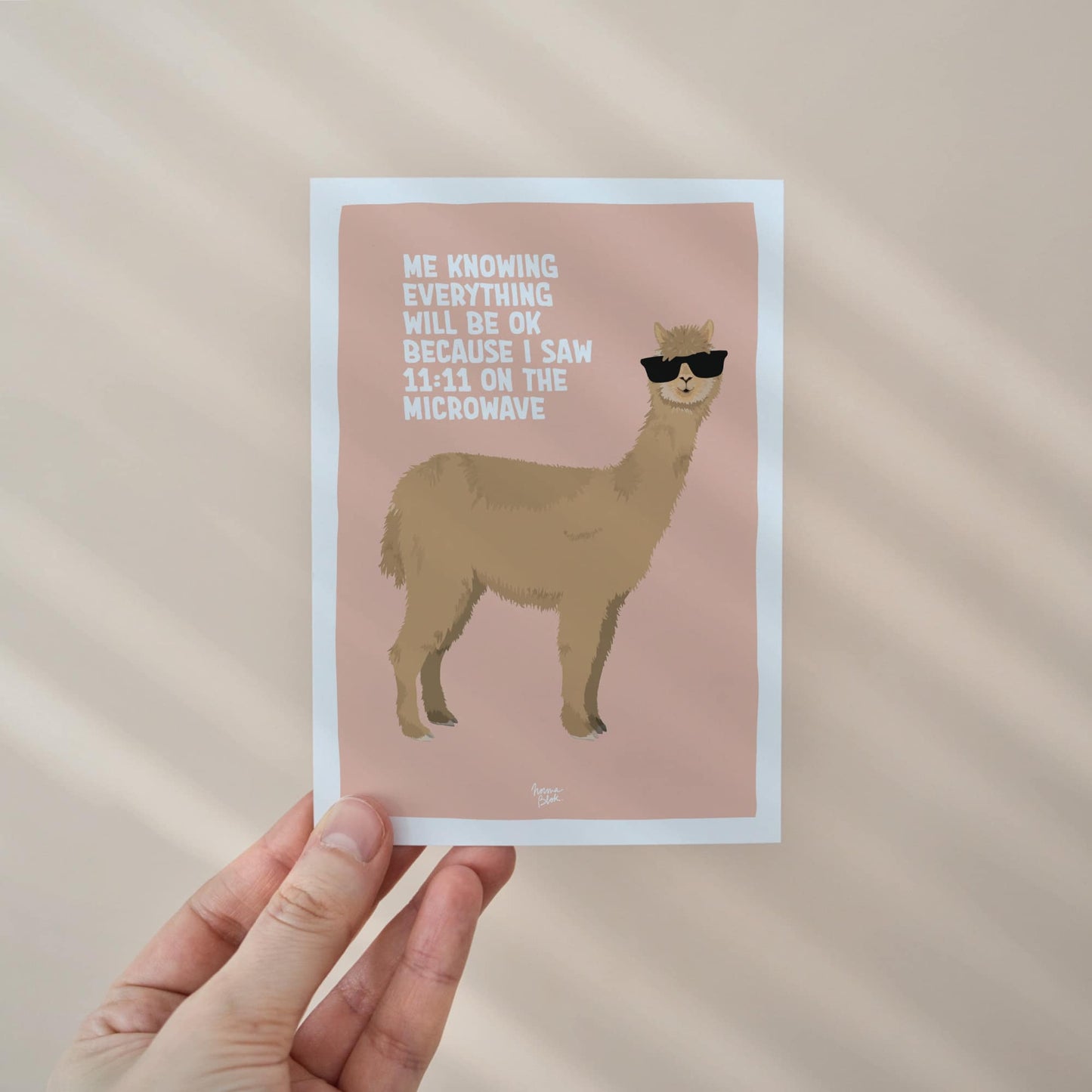 Close-up of a hand holding the alpaca with sunglasses mini print, showcasing the high-quality digital illustration created in Procreate. The image highlights the A6 size and the white border designed for easy framing.