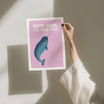 A hand holding the A4 size narwhal art print against a clean white background with a soft wall shadow by Normablok.