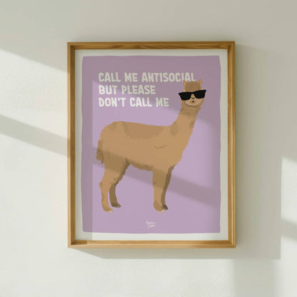The antisocial alpaca art print framed in light wood, hanging on a white wall with natural window light by Normablok.