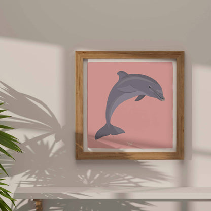The figurative dolphin illustration adapted into a square format layout, framed in natural wood. The minimalist wood frame highlights the soft pink background and creates a contemporary, clean look for any gallery wall.