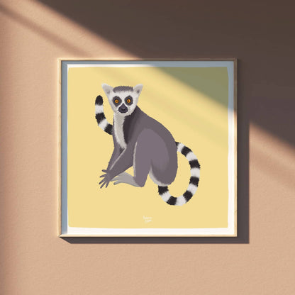 The square-format ring-tailed lemur illustration displayed in a light wooden frame against a soft, sandy beige wall. This minimalist and natural setup highlights how the vibrant yellow background of the lemur print creates a warm, inviting contrast in any modern living space.
