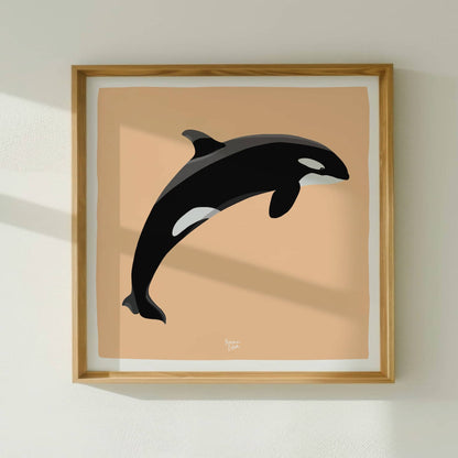 The square-format orca illustration in a clean frame, hung on a plain wall to emphasize the striking color contrast between the black-and-white orca and the orange background.