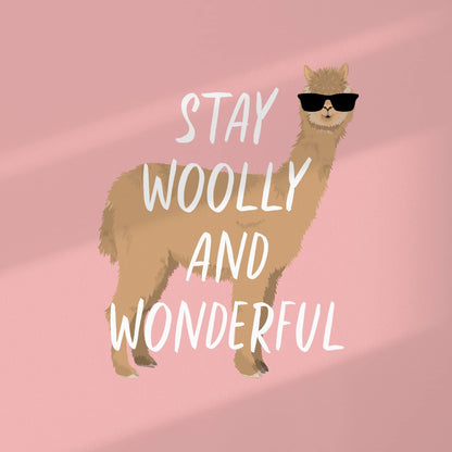 A top-down view of the "Stay Woolly and Wonderful" alpaca art print on a neutral surface. The image highlights the high-quality digital illustration of the alpaca wearing sunglasses against a soft pink background, framed by the signature clean white perimeter border.