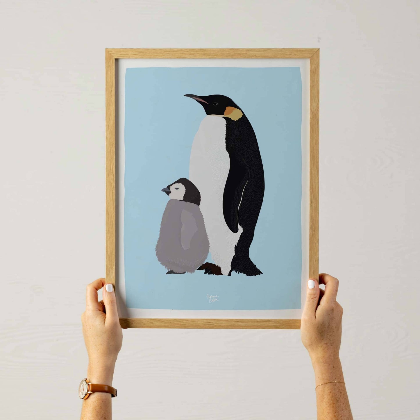 A woman holding an A3 sized framed Emperor penguin illustration, showing the scale for wall decoration.
