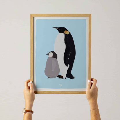 A woman holding an A3 sized framed Emperor penguin illustration, showing the scale for wall decoration.
