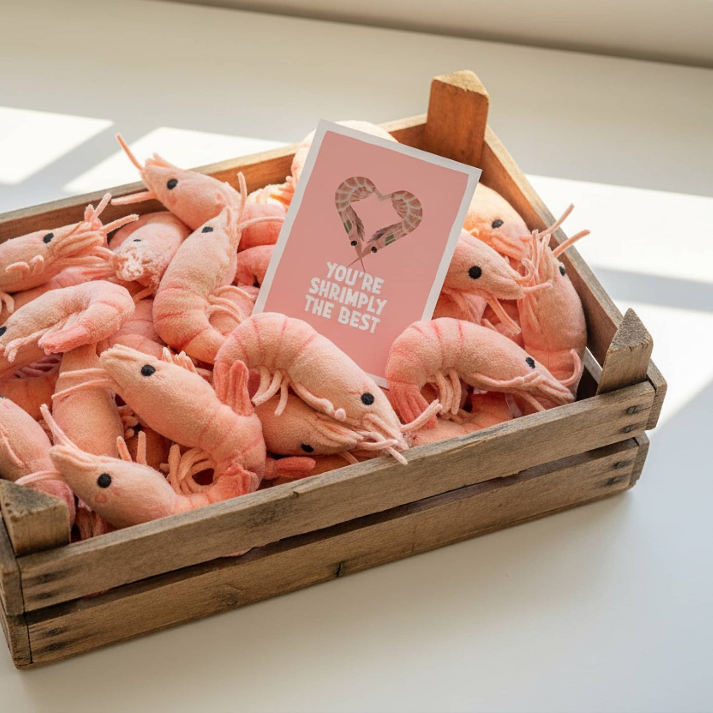 Rustic wooden fishmonger crate filled with plush shrimp stuffed animals, featuring the 'You are shrimply the best' mini art print by normablok.